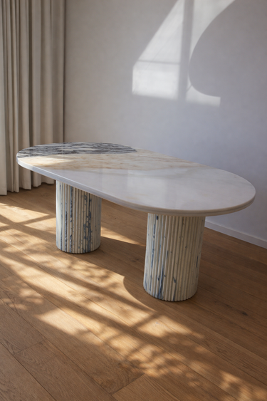 oval dining table in cream marble with natural veining and fluted support